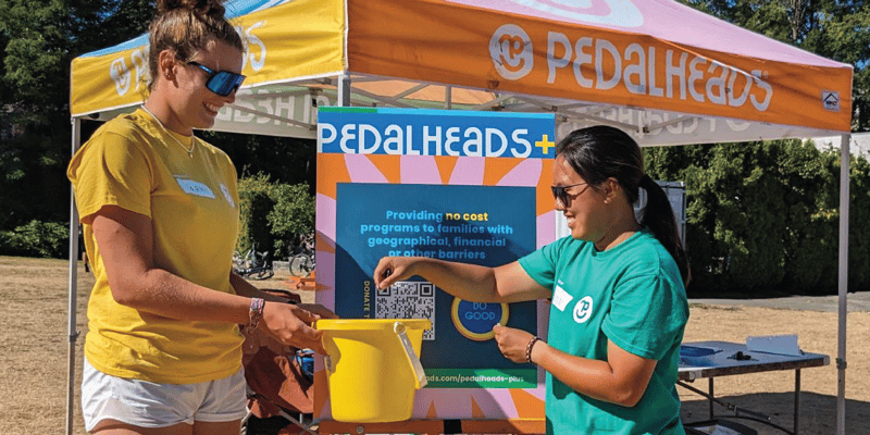 two-pedalheads-instructors-putting-cash-in-a-donation-bin-by-a-pedalheads+-sign